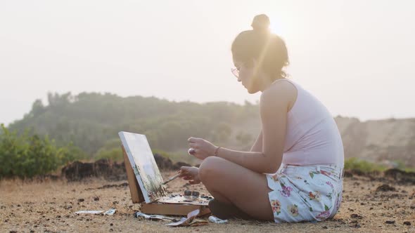 Young Traveler Painting Landscape Picture Sitting Outdoors in Golden Morning Light. Woman Artist