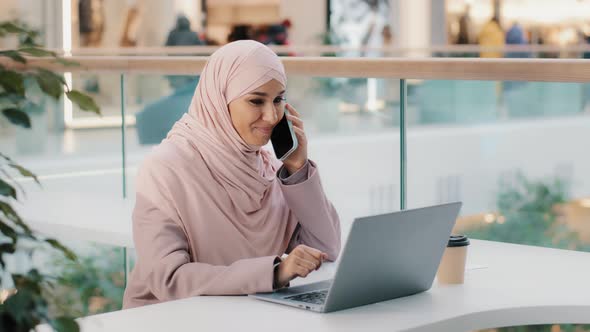 Arab Multitasking Woman Sitting Working on Laptop Talking on Mobile Telephone Remotely Consulting