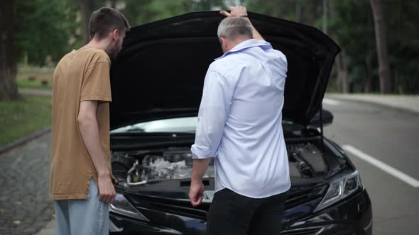 Positive Middle Aged and Young Caucasian Men Closing Car Hood and Giving Highfive