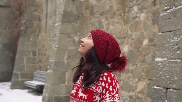 A Happy Female Traveler Looking at the Stone Walls of a Medieval Castle During a Snowfall