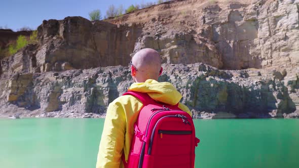 Traveler Examines the Area. View From the Back. Stylish Guy with a Red Backpack Dressed in a Yellow