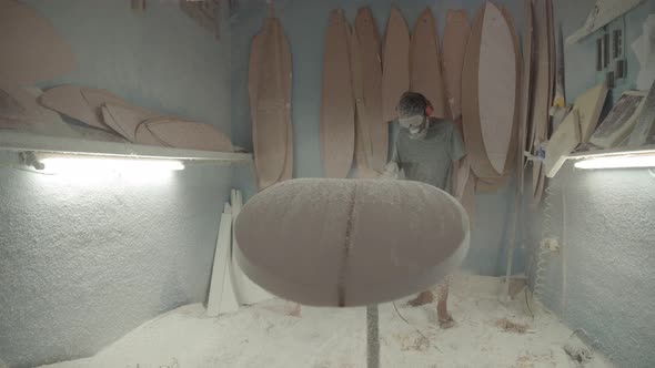 Surfboard Shaper Polishing Surfboard in Workshop