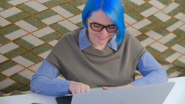 Nerd girl with blue hair working on notebook computer at home during lockdown in 4k video