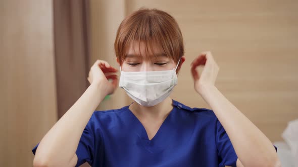 Asian female nurse put protective surgical face mask on to prevent covid virus pandemic in hospital.