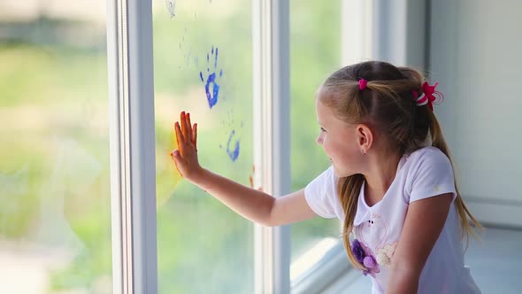 Children girl draw with palms on the window.