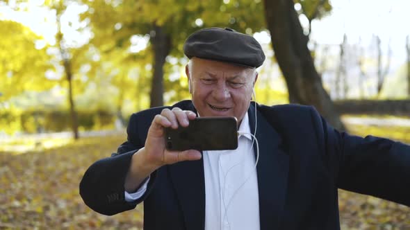 Cheerful Man Having Fun When Talking on Phone Camera Through Earphones Outside