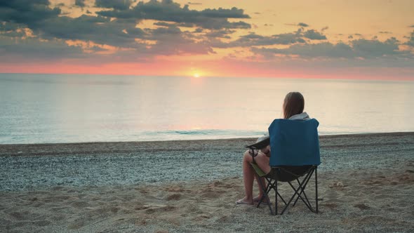 Woman Admiring Sunset on the Sea Sitting in Folding Tourist Chair