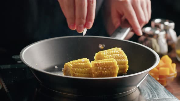 Chef Frying Corn in Pan Adding Salt and Spices Closeup