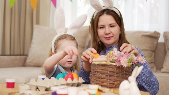 Mom and Little Daughter with Rabbit Ears Celebrate Easter and Lay Painted Eggs