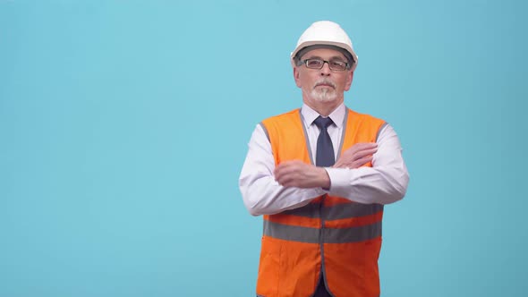 Confident adult engineer in a protective uniform and glasses crosses arms on a blue background