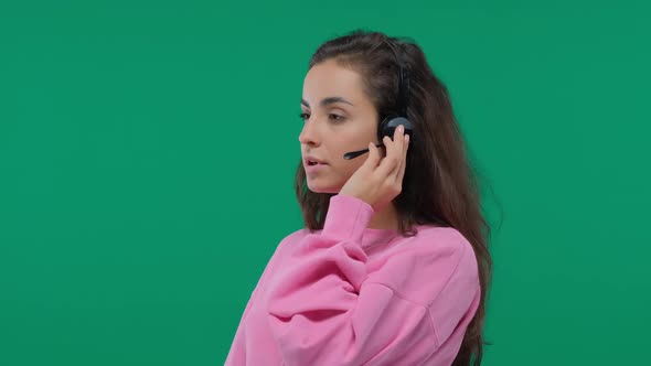 Beautiful Young Woman Consultant with Headphones with Microphone Advises a Client on Green Screen