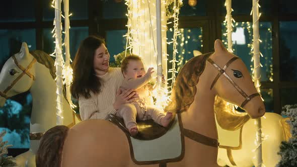 Mom and Baby Play on Carousel with Horses