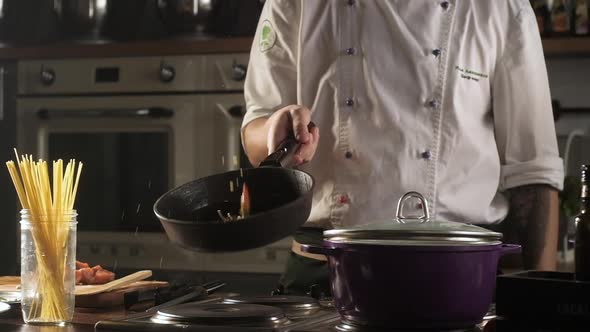 cook in kitchen is frying vegetables in pan and tossing them up.