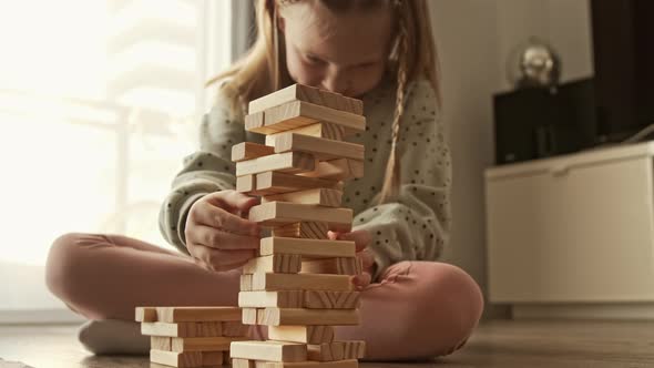 Child plays a board game, kid builds from wooden bricks blocks and the construction tower falls