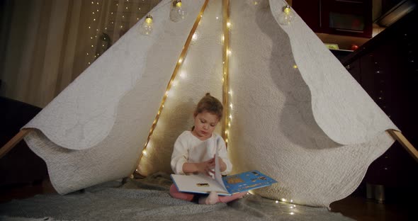 Child in a Wigwam Tent Play at Night and Read a Book