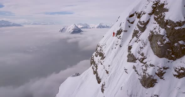 Aerial drone view of a skier skiing down a steep snow covered mountain.