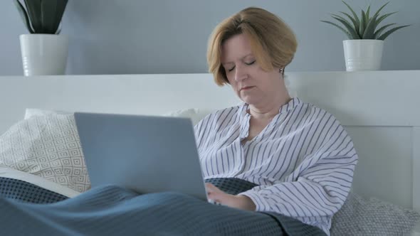 Old Senior Woman Sleeping and Working on Laptop in Bed