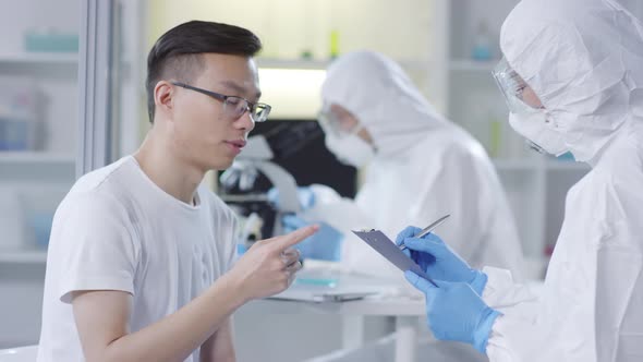 Asian Man Describing Symptoms to Doctor in Disposable Coveralls