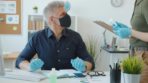 Man in Mask Busy with Computer Work While Employee Taking Temperature with Infrared Thermometer