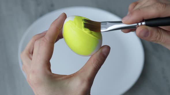 Close-up. Female hands paint Easter egg in a modern minimalist style with colorful paint.