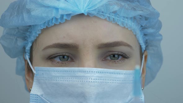 Nurse face in medical mask and cap is holding syringe with Coronavirus vaccine. Virus protection.