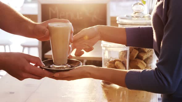 Mid section of waiter serving a cup of cold coffee to customer