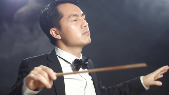 Close Up Side View Of Asian Conductor Man Holding A Baton Closing His Eyes And Showing Gesture