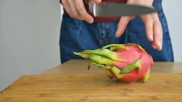 Female Hands is Cutting a Dragon Fruit or Pitaya with Pink Skin and White Pulp with Black Seeds on