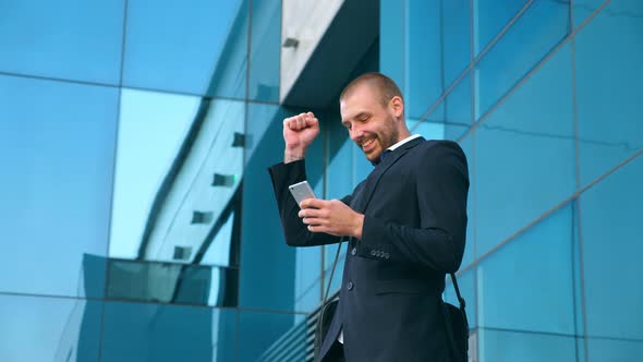 Young Businessman Using Smartphone Near Office and Celebrating Achievement