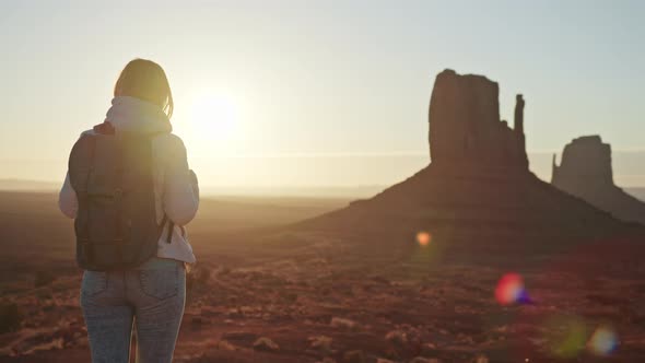 Woman Tourist in Desert Landscape at Sunrise Golden Sunbeams Flare Red Cliffs
