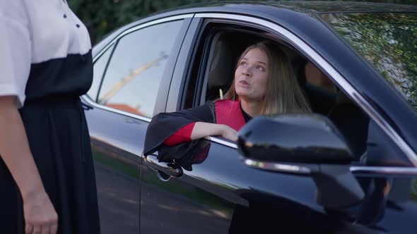 Young Laughing Graduate Woman Sitting in Car Talking with Unrecognizable Parent Outdoors