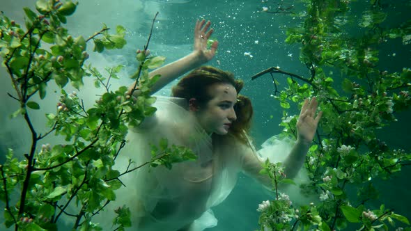 Young Princess is Floating Underwater in Amazing Fabulous Garden Swimming Between Green Trees