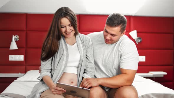 Happy Couple Young Family Enjoying Pregnancy Using Tablet Pc Sitting on Bed Medium Shot