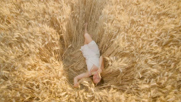 Young Woman Enjoys Relaxing in Ripe Wheat Field on Sunny Day