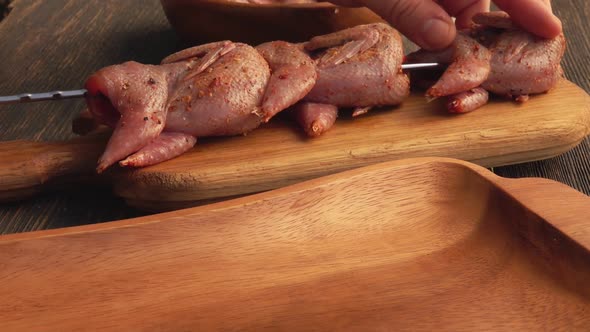 Closeup of Male Hands Piercing Raw Quails on the Skewers on the Wooden Board