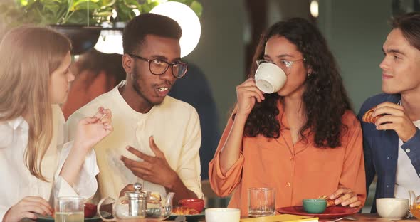 Millennial African American Guy Sharing Idea with Colleagues While They Eating in Cafe, Cheerful