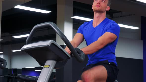 A Young Fit Man Trains on an Exercise Bike in a Gym - Closeup From Below