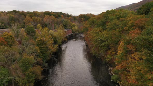 An aerial shot of the colorful fall foliage in upstate NY. The camera dolly in over a black river wi