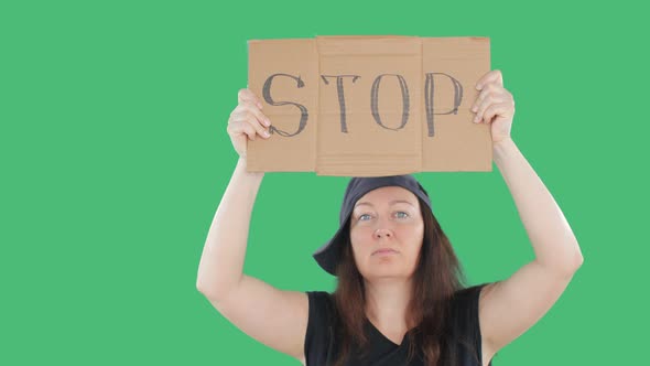 Adult Woman in Cap Showing Cardboard with Stop Sign on Manifestation. Green Background. People