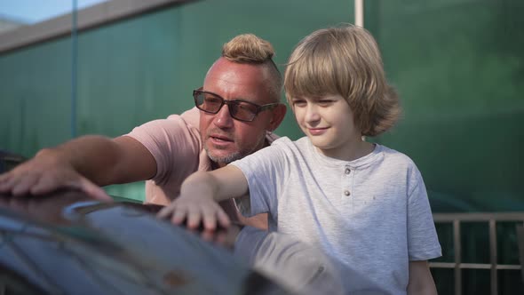 Portrait of Happy Caucasian Father and Son Touching Polished Black Car Talking in Slow Motion