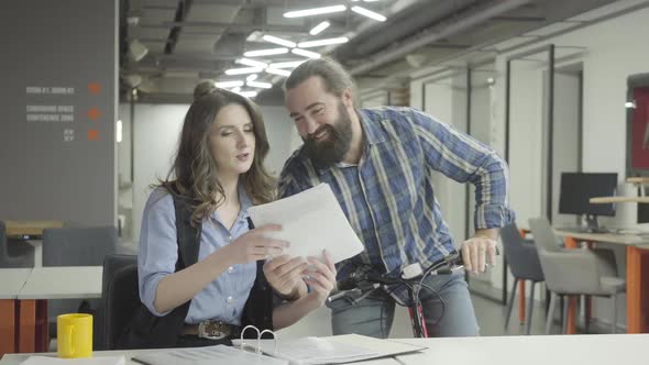 Bearded Smiling Man Rides His Bike with Papers in Hand