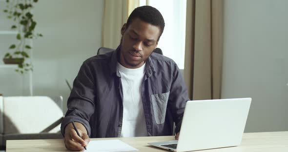 Young Guy Student Pensive Afro American Business Man Freelancer Sits at Table in Front of Laptop