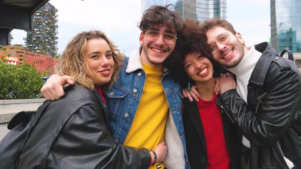 Group of four multiethnic friends outdoor looking at camera hugging laughing