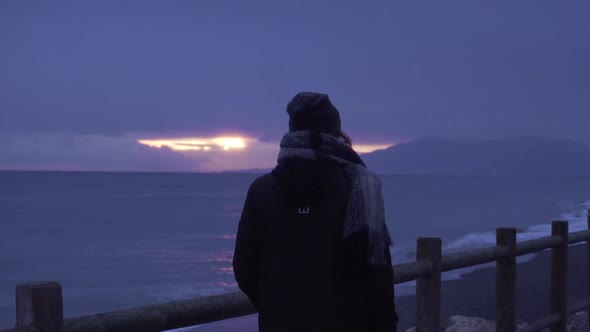 Woman with winter clothes looking at sea at twilight
