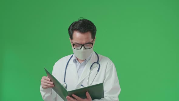 Asian Doctor With Stethoscope Wearing Mask, Reading Document While Walking On Green Screen