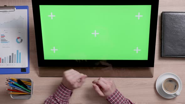 Top View of a Man's Hands Touch the Bottom Left Corner of a Green Screen on Touch Monitor