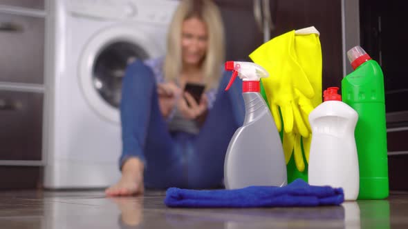 woman sitting on floor with her phone out of focus. Bottles of cleaning agent