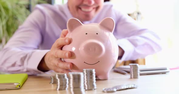 Smiling Businesswoman Strokes and Shakes Piggy Bank with Coins