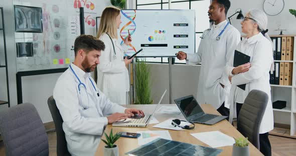 Doctor Working on Laptop While Another Male and Female Colleagues Discussing DNA