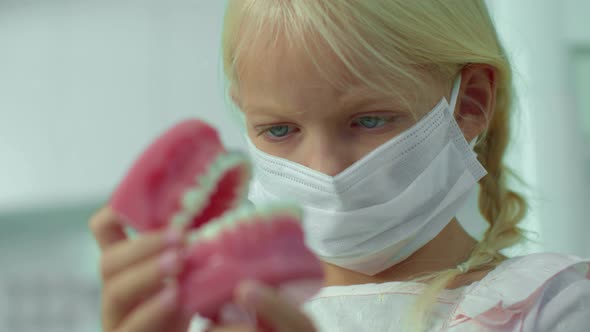 Girl in Mask Is Looking at Medical Jawbone.